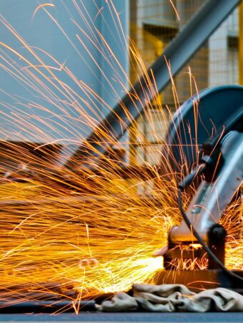 A worker operates a grinder cutting metal, creating a vibrant display of sparks in an industrial setting.